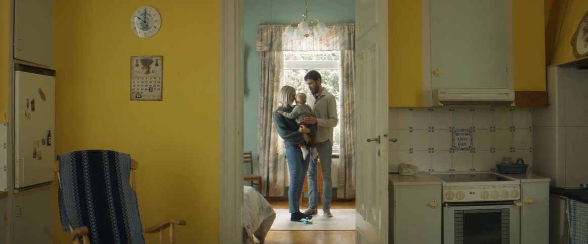 A woman holds her baby as she hugs her husband while standing in a room near their kitchen