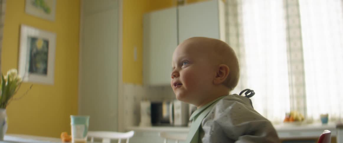 Toddler sitting at kitchen table smiles and laughs