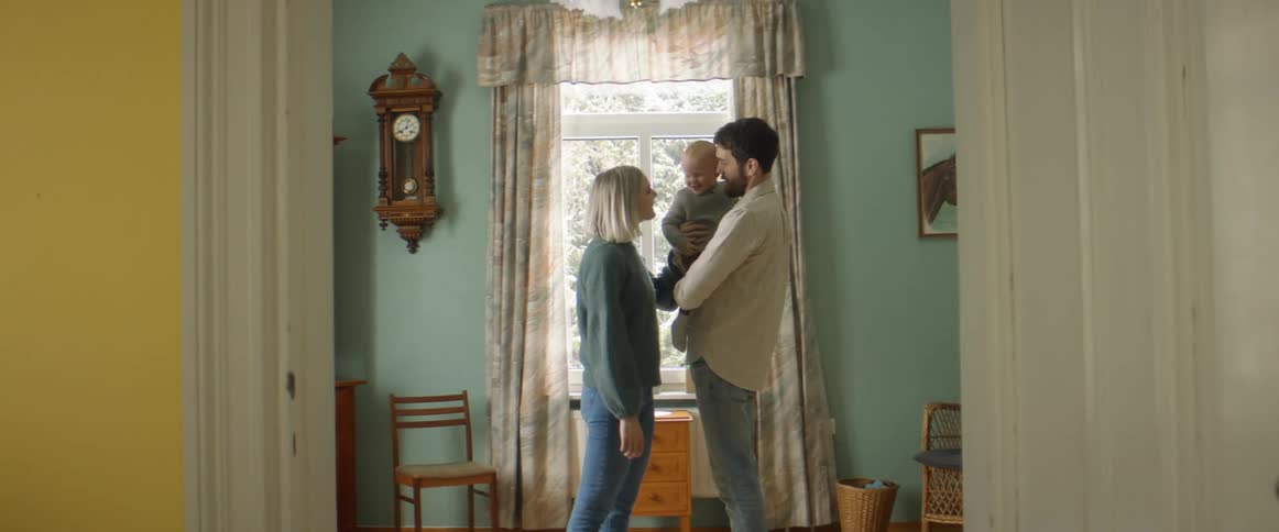 A dad holds his baby son while mom talks and smiles