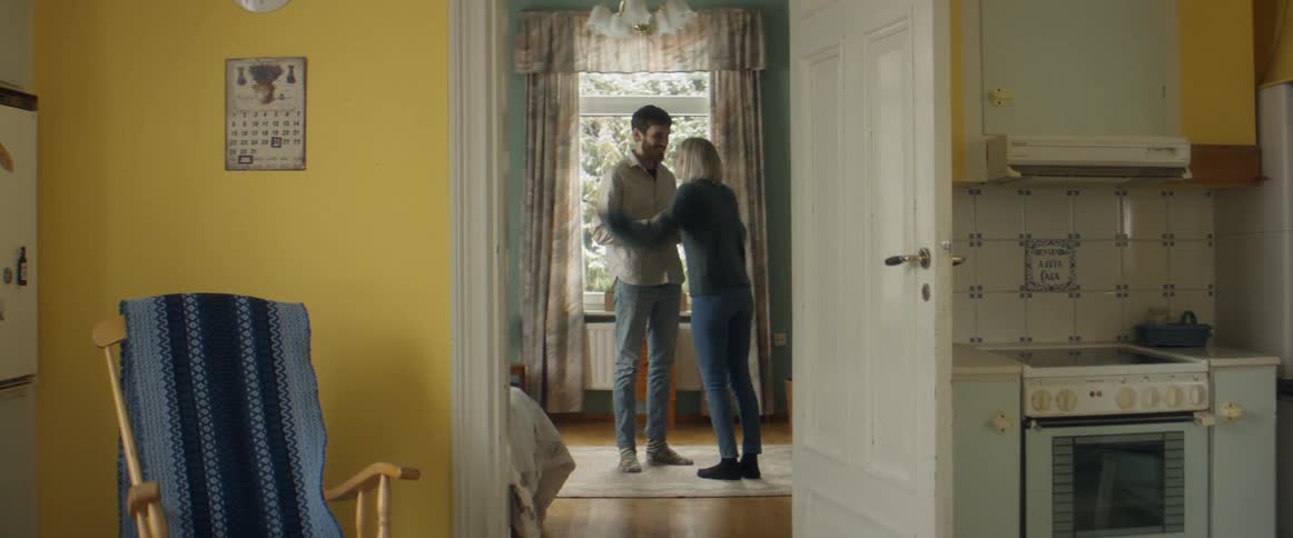 A woman runs through the kitchen to surprise her husband with a pregnancy test result