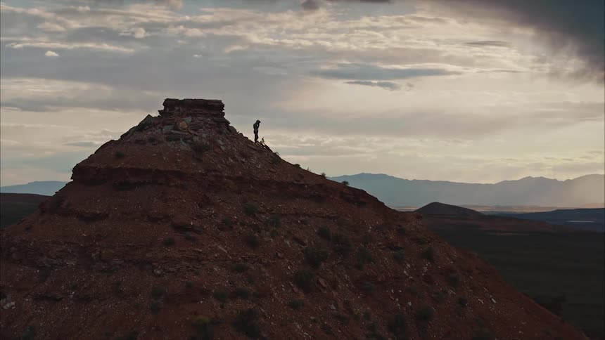 A mountain biker prepares to drop into a run from the top of a mountain under stormy desert skies