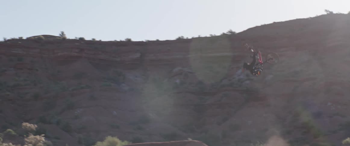 A mountain biker back flips a desert jump in the air before successfully landing on the other side in the badlands during the day