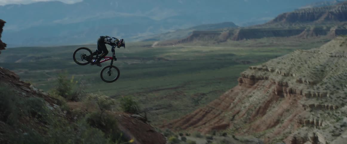 A person on a mountain bike dropping of a cliff in front of desert valley
