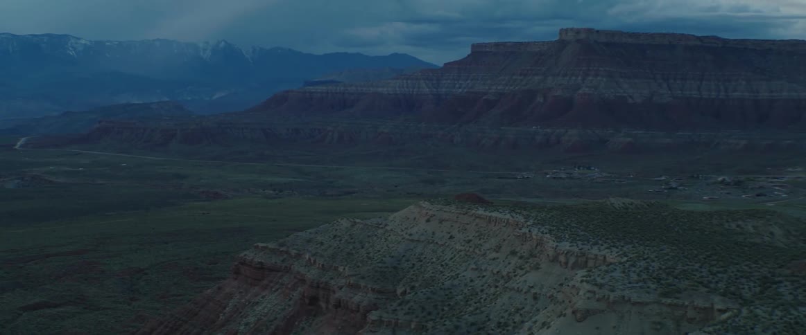 Views across the desert valley towards mountains and a mesa at stormy dusk