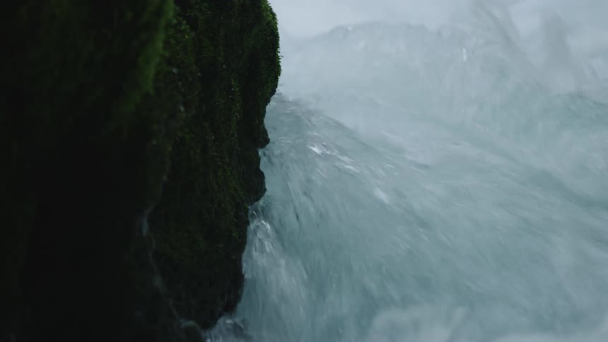 Whitewater flows past moss covered dark rock in this real time shot communicating a pristine scene