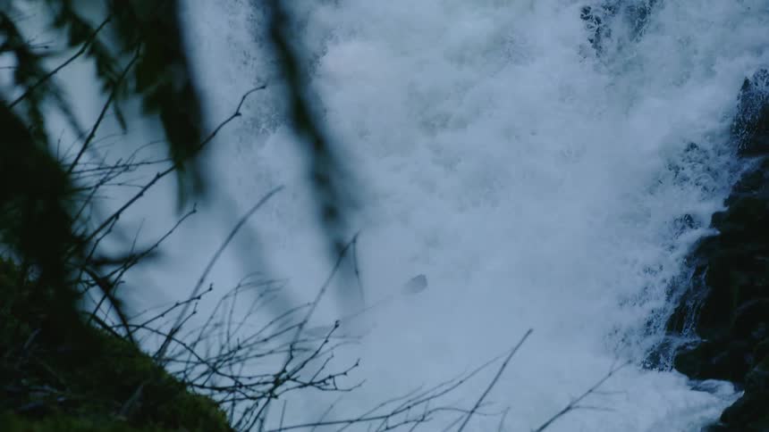 Slow motion tight shot of a man in a red kayak paddling over the lip of a large whitewater waterfall in the pacific northwest