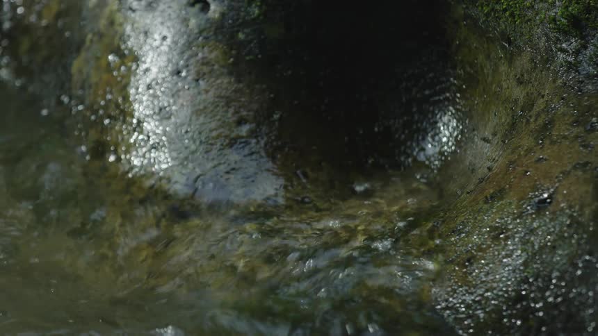 River water washes up and splashes against polished granite rock on the side of the river showing the passage of time and permanence of earth