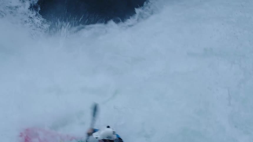 Real time shot of a man in a red whitewater kayak launching over the lip of a strong rapid and almost getting recirculated in the falls below before looking at the camera and laughing