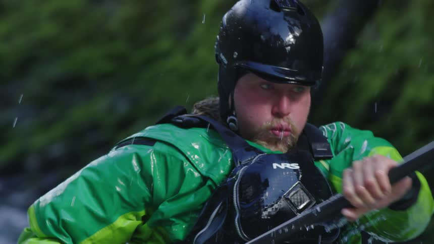 Slow motion tight shot of a bearded man paddling fast and hard in a whitewater kayak before leaving frame