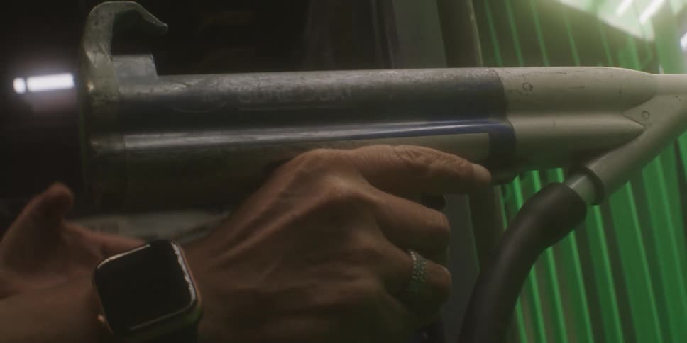 A person with a watch in a room using a tool with a hose