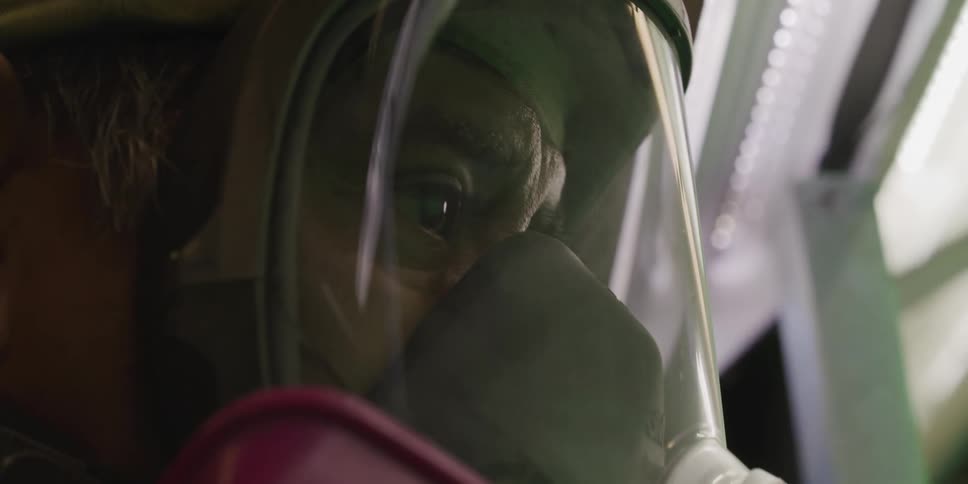 A man wears a gas mask as he stands under bright lights in a room