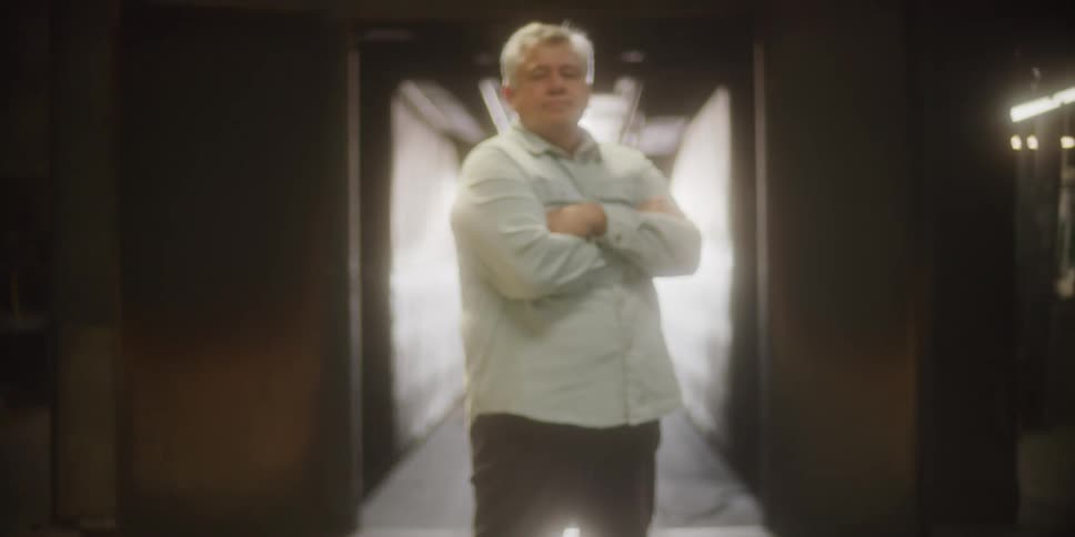 A man stand at the entrance of a hallway and crosses his arms over his chest