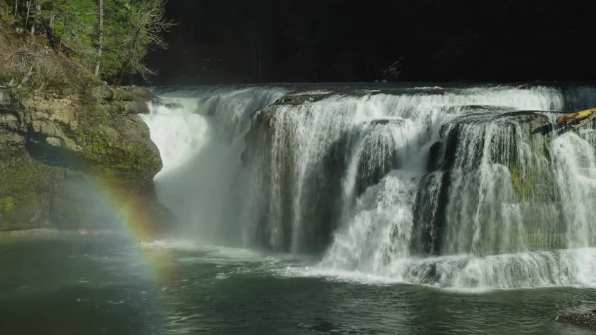 A massive waterfall crashes into the calm pool below creating mist that reflects making a wonderful rainbow in the foreground