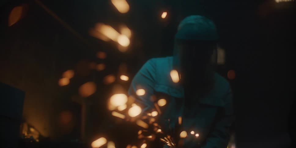 A person with a welding helmet in a workshop welding with sparks with a wall in the background