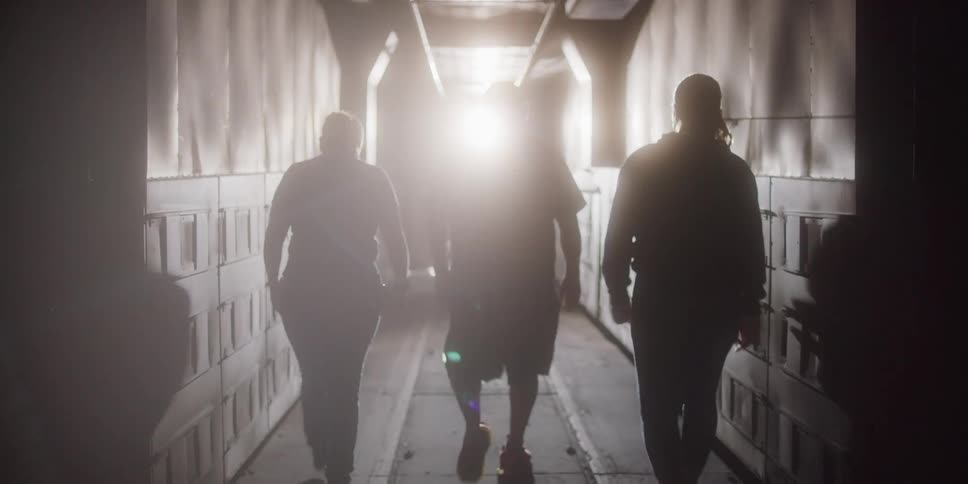 Three silhouetted people walking down a corridor with a bright light