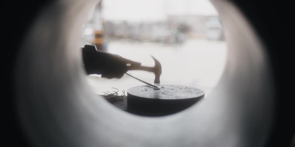 A construction worker hammers a barrel white seated next to a wide pipe