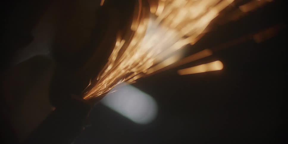 Sparks flying from a metal grinder inside a dark workshop