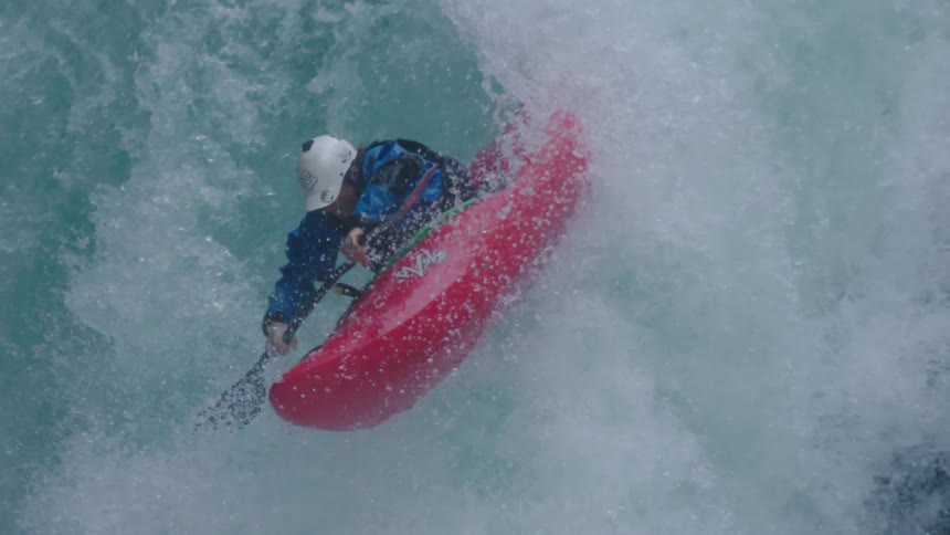 Slow motion tight shot of a man in a red whitewater kayak paddling over a large waterfall and paddling away from frame after landing