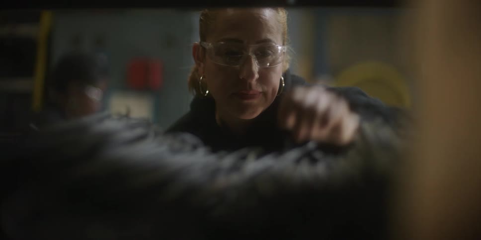 A woman chooses long thin pieces of metal from a shelf filled with metal
