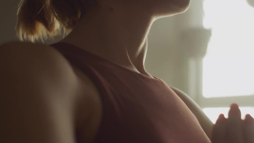 A woman in a room stretching with a wall and window in the background