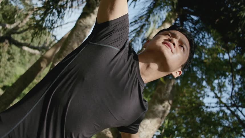 A man stretching with his arms out near trees outside