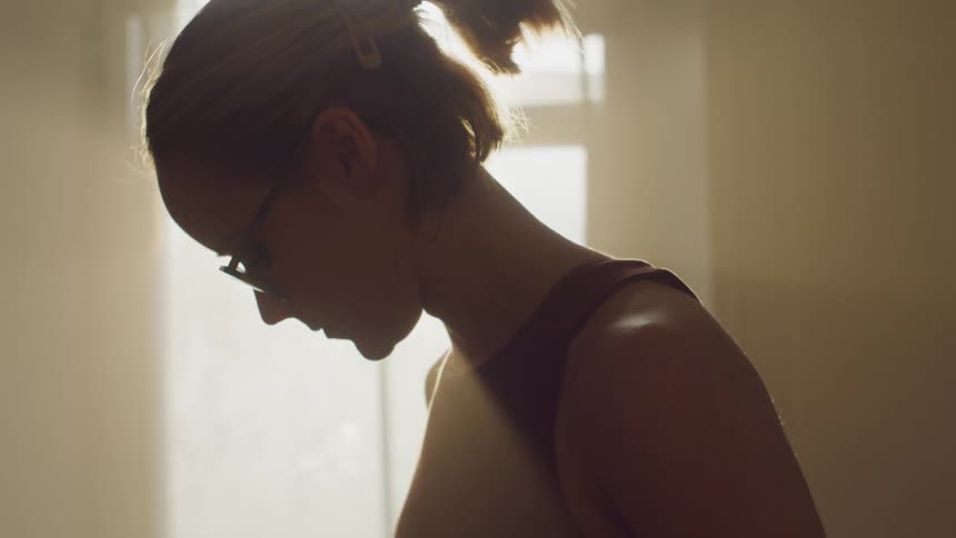 A woman stands in front of a window at home as the sun shines in