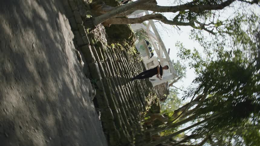 A male performs a ballet dance move on a stone staircase in between trees outdoors at daytime