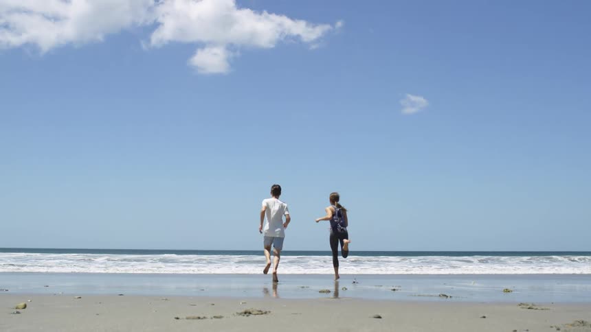 Two teenagers running over the wet sand next to the ocean