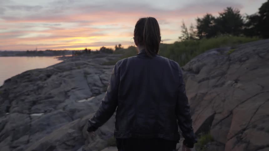A woman is walking along rocks by the shore