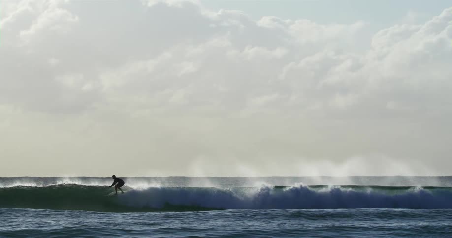 A surfer rides a splashing wave under a cloudy sky