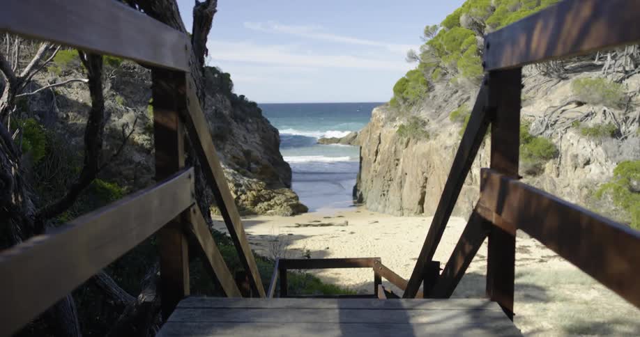 A staircase with a banister with the beach the sky and clouds in the background