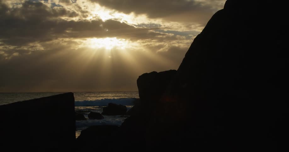 The sunlight is streaming down through the clouds onto the waves at the shoreline