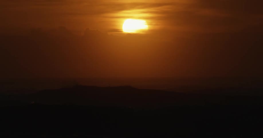 The sun glowing amber behind the clouds