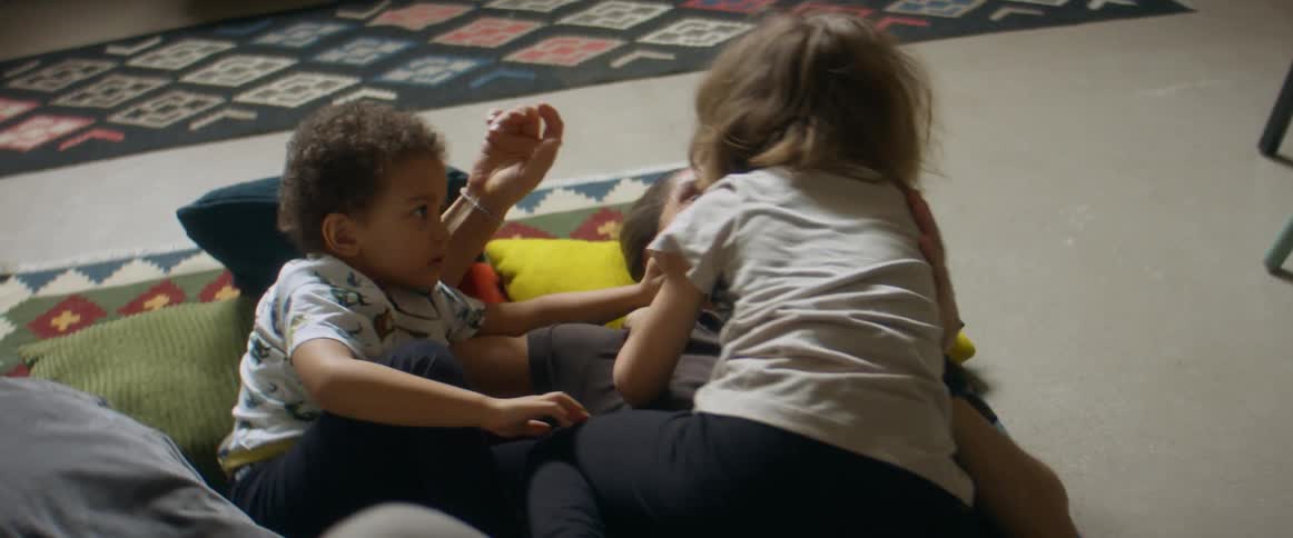 A man laughs as she rolls on the floor with his children