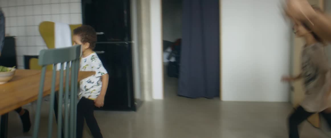 A dad chases two children around the home dining table