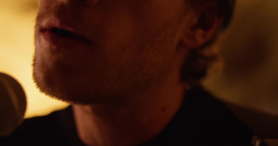 A male performer singing into a microphone while wearing sunglasses in a dark room
