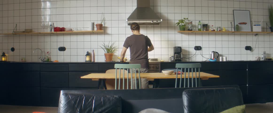 Children running in a room with a person cooking on a stove in the background