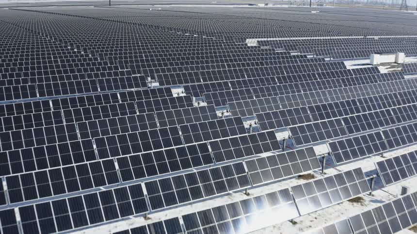 Solar farm with many solar panels with snow on the ground and utility towers in the distance