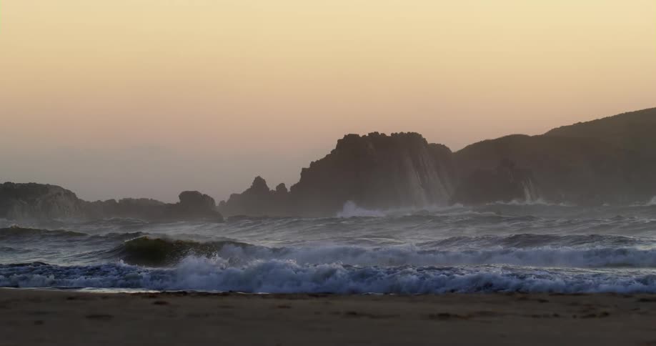 Ocean waves roll into a sandy beach at sunset