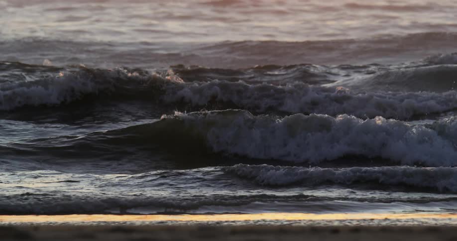 Reflected sun fades from water on beach as waves roll onto shore