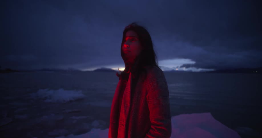 A woman standing by a lake with glaciers with the sky and clouds in the background