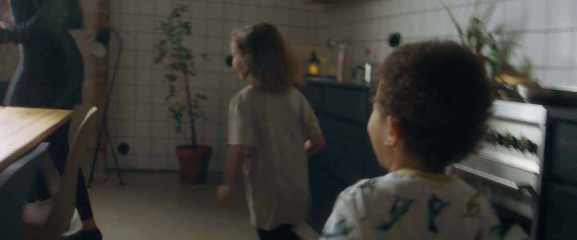 A mother and a father playing with their two small children chasing them around a dining room table at home during the day