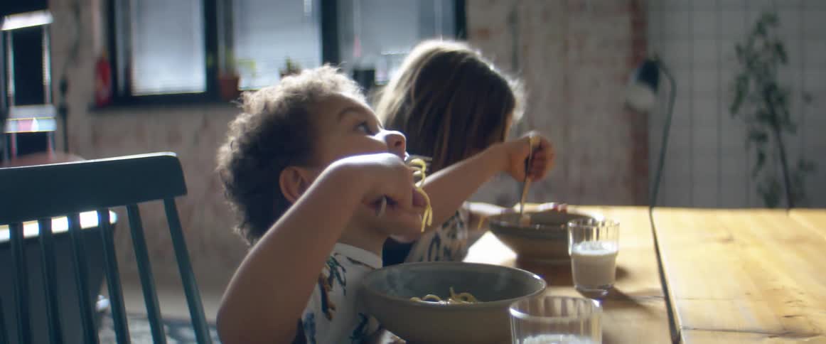 Two young children sit at a table eating spaghetti