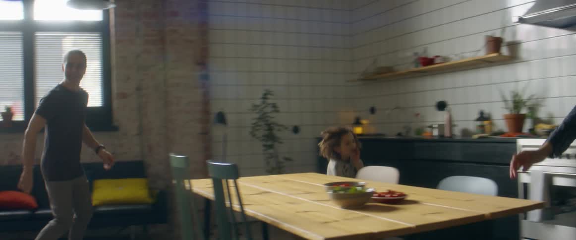 A man a woman a boy and a girl running around a table and chairs in a room