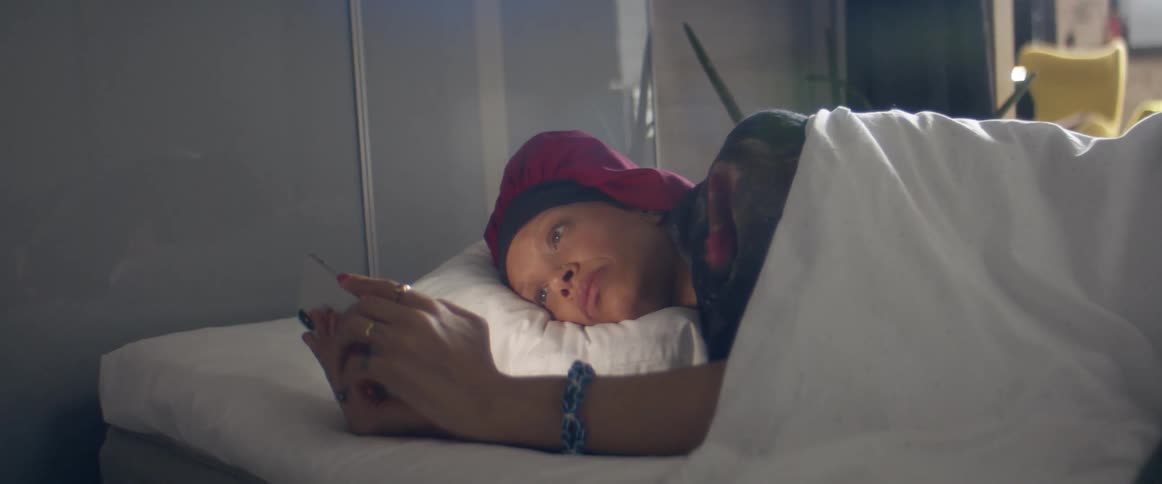 A woman lies in bed and looks at her cell phone