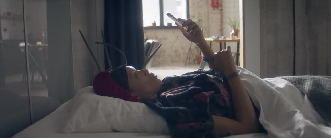 A woman looking at a smartphone while feeling ill in bed