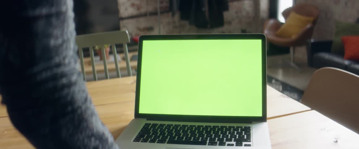 A person in a room looking at a laptop on a table with a chair and couch in the background