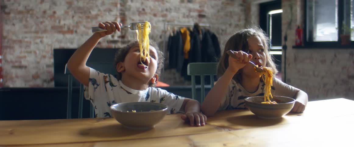 Two kids eating pasta at a table