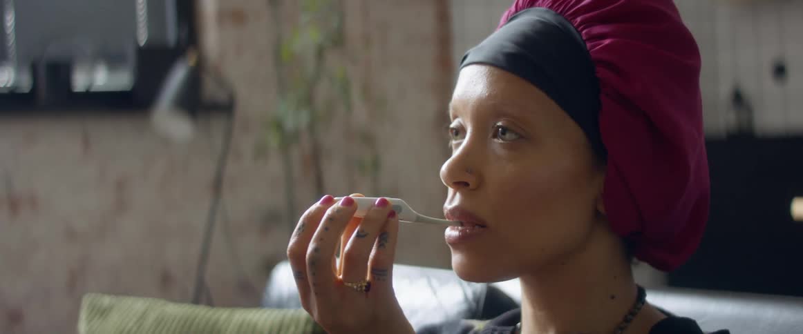 A woman takes her temperature as she sits on her couch