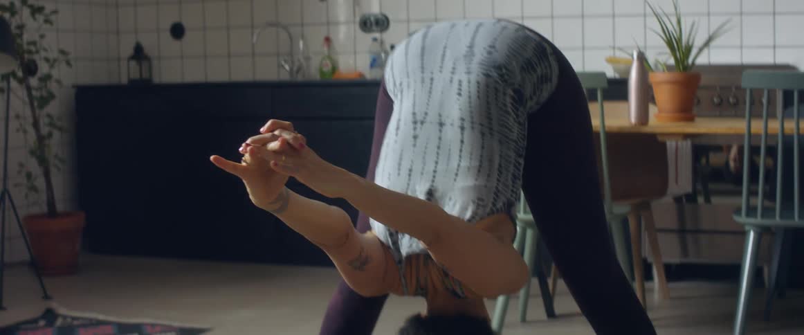 A woman bent over stretching and holding yoga poses on an area rug near her kitchen